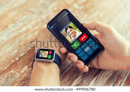business, technology and people concept - close up of male hand holding smart phone and wearing smart watch with incoming call interface on screen