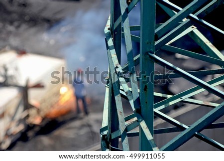 Abstract image industrial area in the port with carpenters at work. In the foreground, bearing structure of an electricity pylon and in the background a worker with blowtorch. 