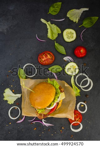 Tasty street food grilled beef burger in crispy shortbread with lettuce and fresh vegetables on stone dark background.