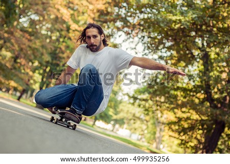 Skateboarder squatting on a skateboard and ride a slope on the road through the forest. Freeride skateboarding