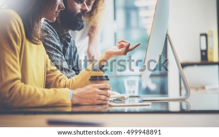 Group of three young coworkers working together in a sunny office.Man typing on computer keyboard.Woman pointing hand to desktop screen.Horizontal image,blurred background