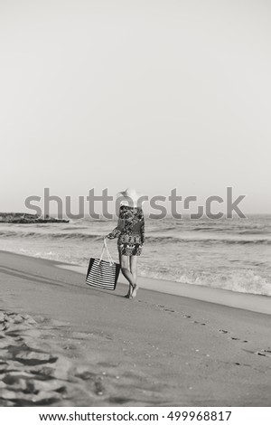Back side view of woman in summer hat and beach bag walking on the sunny ocean tropic outdoors background