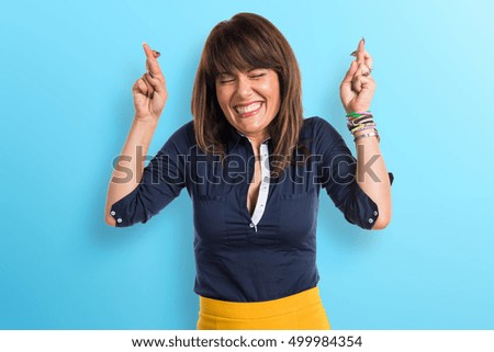 Pretty woman with her fingers crossing over blue background
