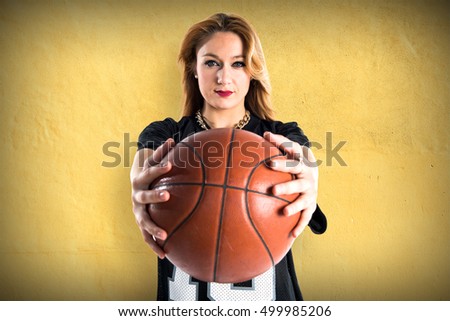Blonde pretty woman playing basketball over textured background