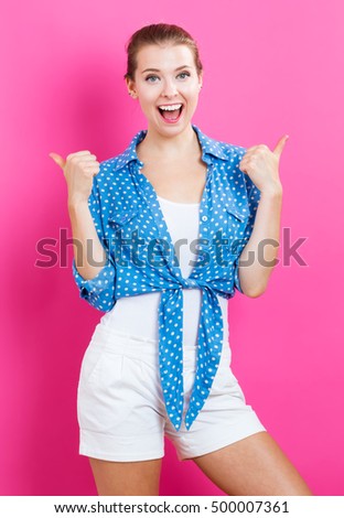 Happy young woman giving thumbs up on pink background