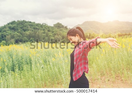 Young happy woman raising hands in yellow flower field on sunset,mountain view backgound.