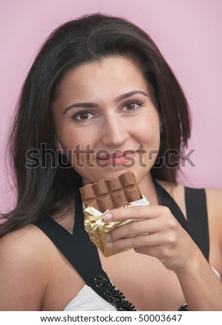 Beautiful young woman with chocolate bar on pink background