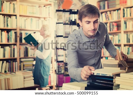 Adult smiling man choosing new book from many in book shop
