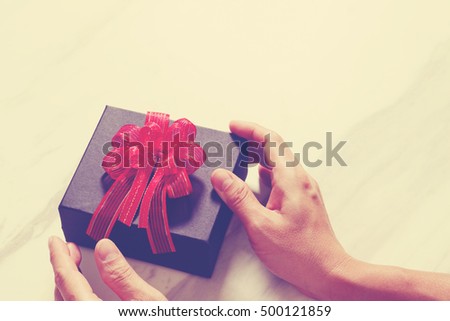 man hand holding a gift box in a gesture of giving on white gray marble table background,vintage

