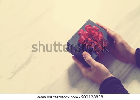 man hand holding a gift box in a gesture of giving on white gray marble table background,vintage