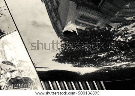 Autumn in Paris.Faded leaf and typical Parisian building reflection on the car surface. Black and white.