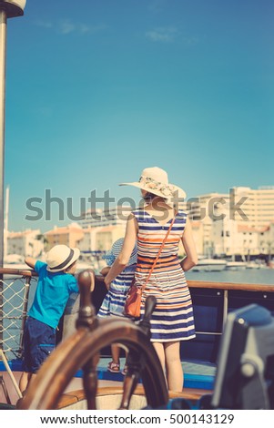 Closeup on steering wheel of sailing ship and back view of mother with kids. Sunny blue sky outdoors background. Book cover idea design