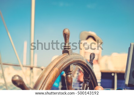 Closeup on steering wheel of sailing ship and back view of mother with kids. Sunny blue sky outdoors background. Book cover idea design