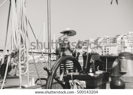 Closeup on steering wheel of sailing ship and back view of mother with kids. Sunny sky outdoors background. Book cover idea design. Black and white photography