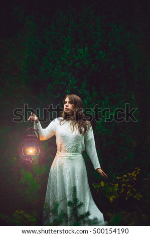 Beautiful girl in white holding a lantern in the autumn forest on a green background