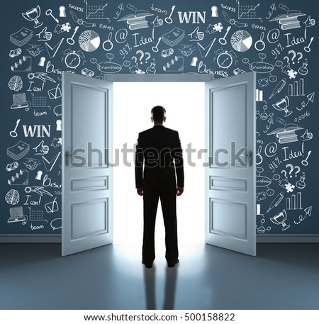 Back view of young businessman standing in room with business icons on wall against open door with bright light. Success concept