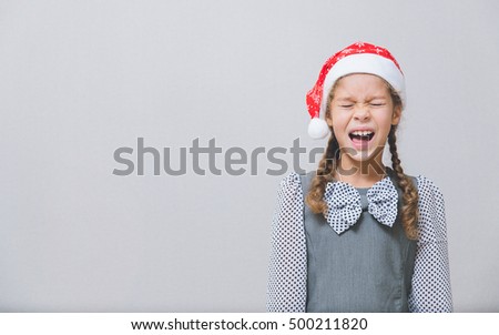 Christmas theme. Multi-ethnic girl in santa claus really wants gifts. Gray background. 