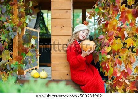 Little beautiful girl sitting at backyard of house with pumpkins ready to celebrate Halloween and meet autumn