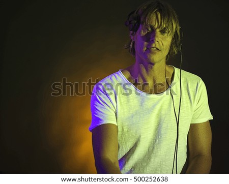 Portrait of handsome blonde DJ in headphones looking at camera while at turntable mixing music at party.