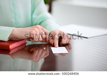 Business woman hands in a green blouse sitting at a desk in an office and holds out business card.
