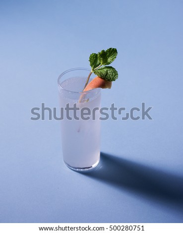 A photograph of gin and tonic that contains bright garnishes on the lip of glass. The shot is from above the high ball glass, with a dark shadow that's cast on the blue background.