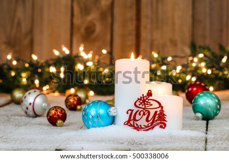 Christmas background with white candles, holiday ornaments, the word Joy and string of lights with green garland border in snow; red, teal blue, silver and gold rustic Christmas background