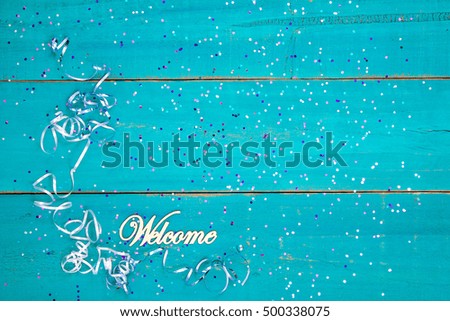Welcome sign with colorful holiday confetti and ribbon border on blank antique rustic teal blue textured wood background sign; color copy space for text with pink, purple, blue decorations