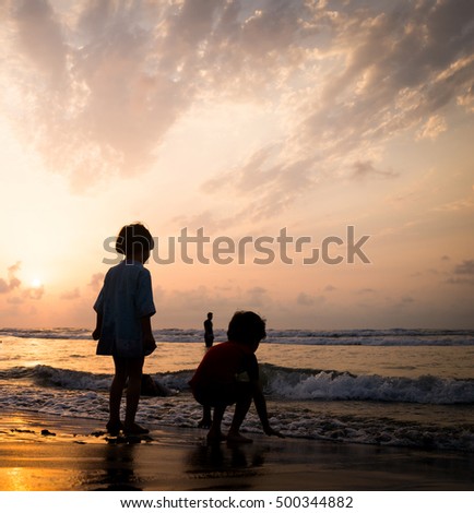 Kids silhouettes having happy time on sea beach near sunset