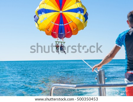 Happy couple Parasailing in Dominicana beach in summer. Couple under parachute hanging mid air. Having fun. Tropical Paradise. Positive human emotions, feelings, family, children, travel, vacation. Royalty-Free Stock Photo #500350453