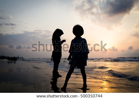 Kids silhouettes having happy time on sea beach near sunset