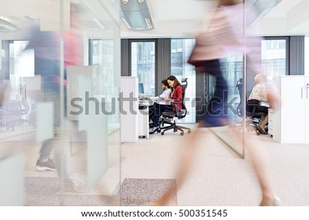 Blurred motion of businesswoman walking with colleagues working in background at office