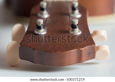 Close up of the head and tuners of a dark brown ukulele, with four black strings attached to it.
