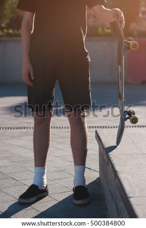 Guy holding skateboard. Skateboarder wears shorts. Developing talent takes time. From simple to difficult.