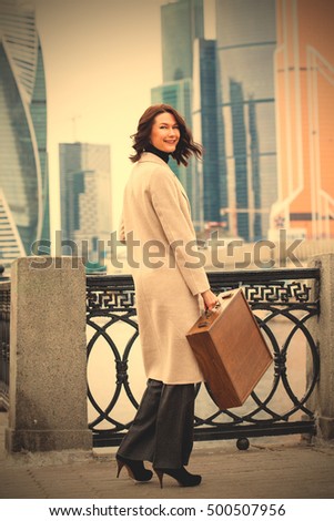 smiling woman in a bright coat with wooden case in her hand on the background of the business district skyline. businesswoman. designer. architect. fashion. instagram image filter retro style