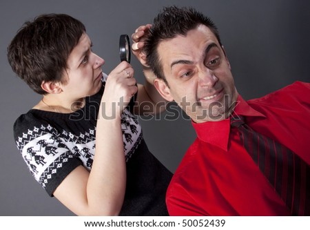 Woman examining man's hair with magnifying glass