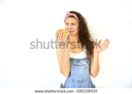 beautiful hipster girl is holding a burger and make faces. Model isolated on white background