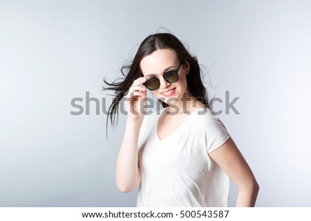 Attractive young woman in sunglasses posing on gray wall.