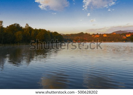 Mountain lake for fishing against the background of green vegetation, blue morning sky in cirrus clouds and the rising sun. Early morning. Western Ukraine.