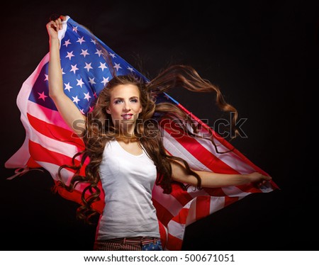 Young attractive girl holding a waving US flag. She a T-shirt and shorts with a print of the flag. Long curly hair. Patriot country.