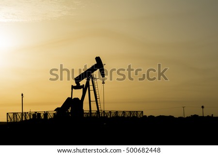 Silhouette of crude oil pump in oilfield at sunset 