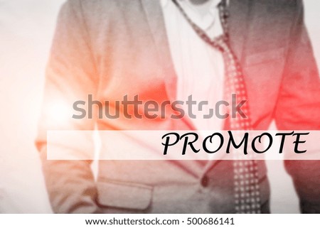 Hand writing PROMOTE with the young business man on background. Business concept. Stock Photo.