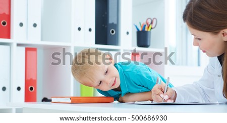 Little boy watching the doctor adds the value to the medical form.