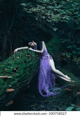 Sleeping Beauty lies on a log. Background fairy forest. Sad Princess, crying. Luxury purple dress. Fashionable toning