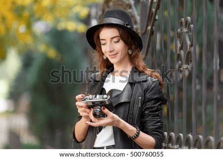 Young woman holding the camera outdoors. Beautiful hipster girl shooting with retro camera. In the autumn sunny day, beautiful girl hipster in a hat photographed on the city street