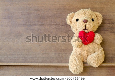 Teddy bear holding a heart-shaped pillow on wood shelf board background