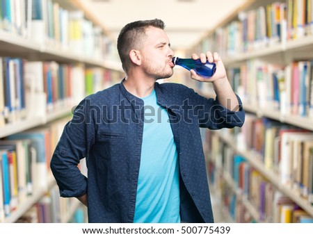 Young man wearing a blue outfit. Drinking water. Over library background.