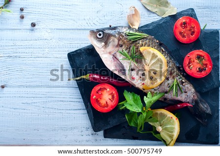 Raw fresh river fish fish on plate cutting board. Fish, lemon, tomato, herbs and spices. Top view with copy space on stone table
