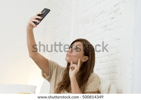 young attractive 30 years old woman playing on home sofa couch taking selfie portrait with mobile phone having fun laughing and smiling happy and playful 
