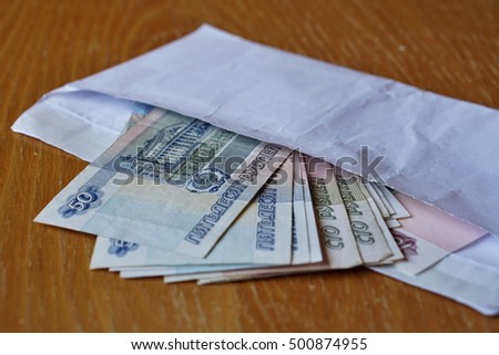 White envelope full of Russian currency (Russian Ruble, RUB) on the wooden table as a symbol of cash transfer, money laundering or bribery in Russia