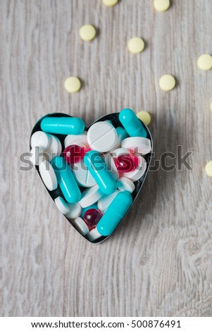 Heart from colorful medication and pills from above on grey wooden background. Copy space. Top view, frame. Painkillers, tablets, generic pills, drugs. 
